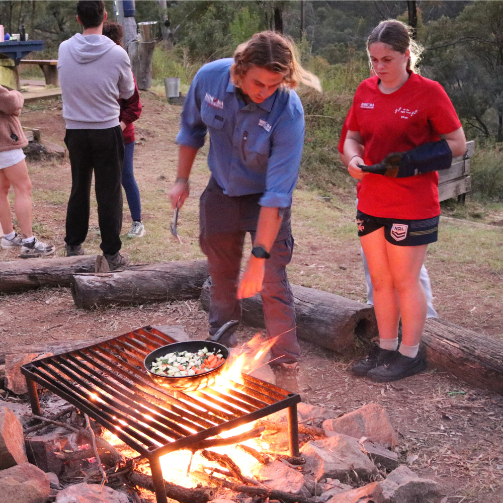 Youth Worker teaching student how to cook over open fire
