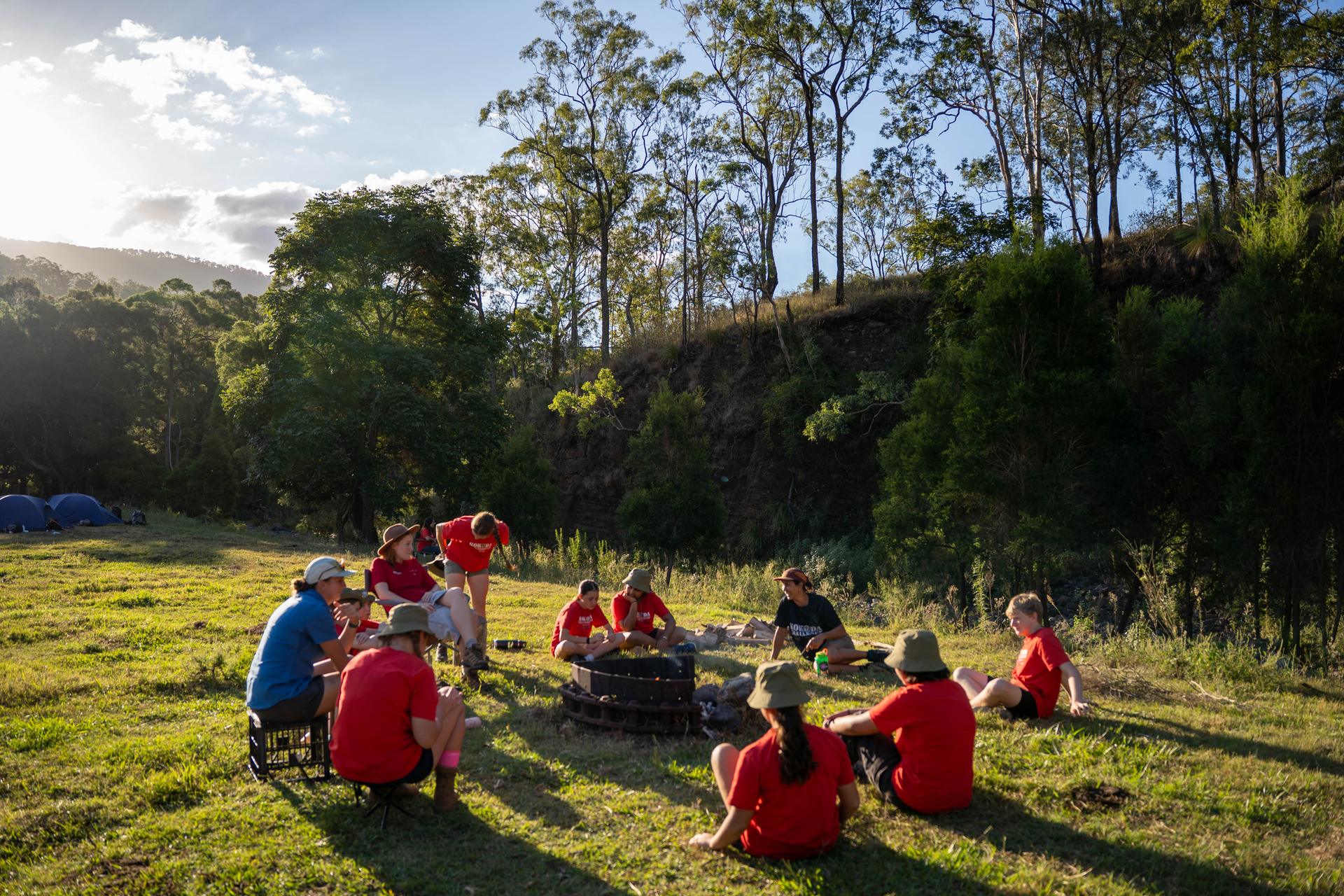 A group gathered around the campfire circle at Kokoda Park in late afternoon light